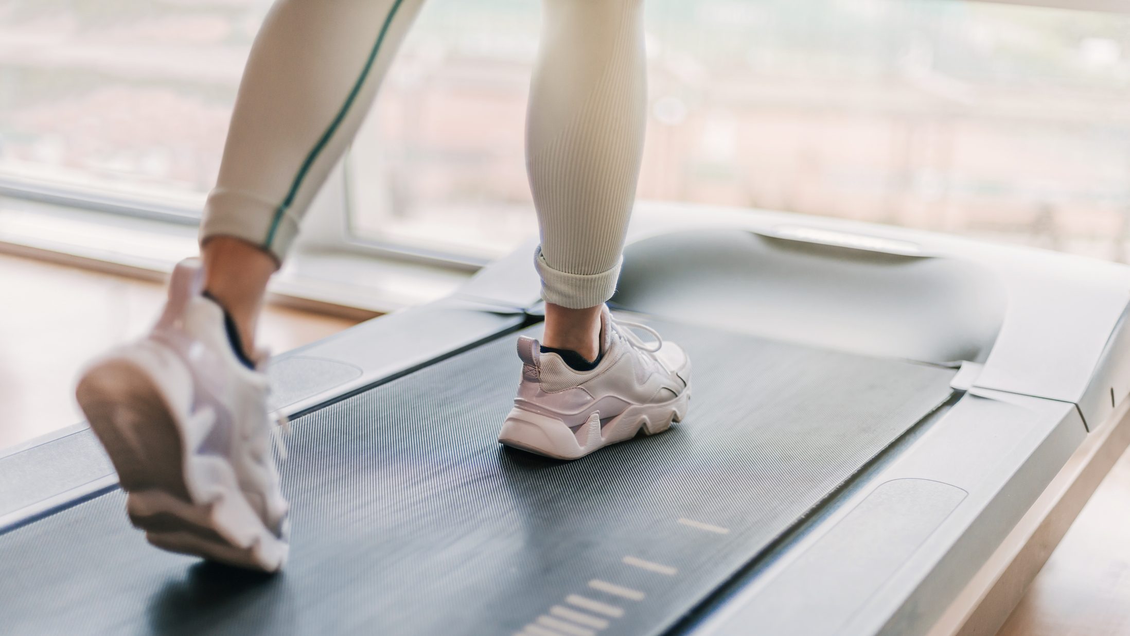 selectively blurred detail of legs running on a treadmill. a warm light enters through the window in the background.