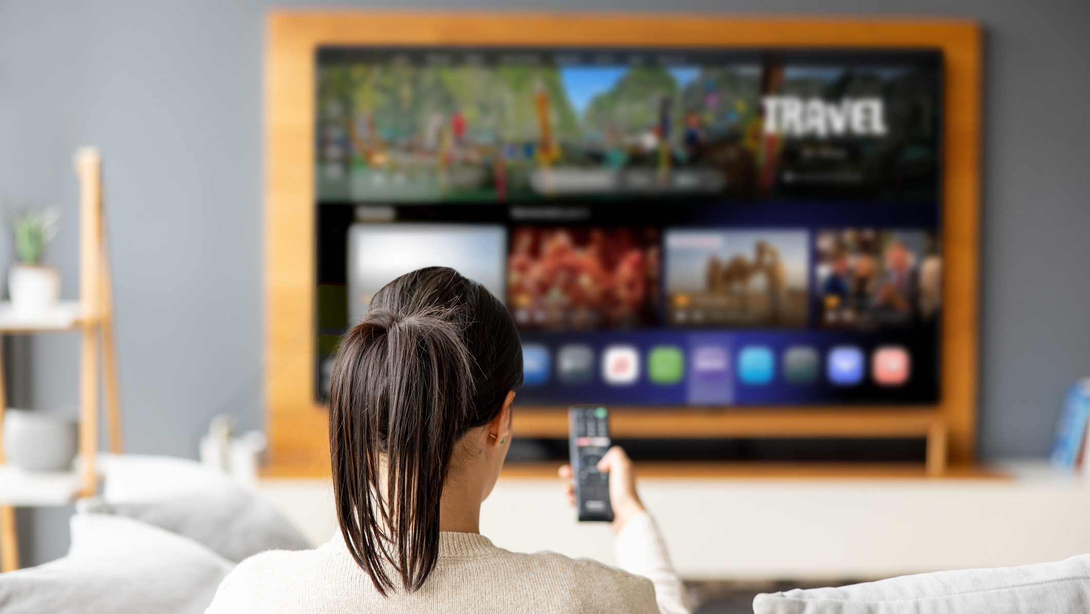 Woman at home holding the remote control while watching a travel channel on the TV - streaming service concepts