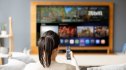 Woman at home holding the remote control while watching a travel channel on the TV - streaming service concepts